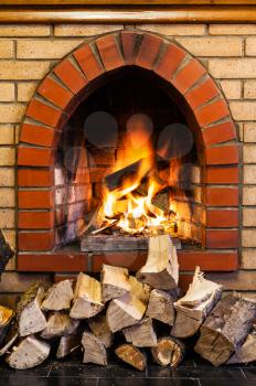 stack of wood and fire in indoor brick fireplace in country cottage
