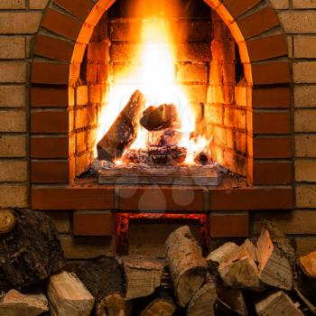 stack of wood and tongues of fire in indoor brick fireplace in country cottage