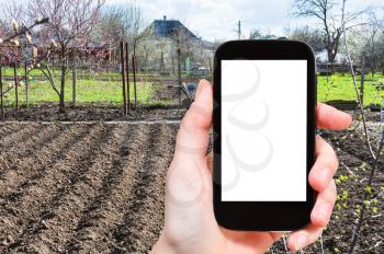 season concept - farmer photographs plowed vegetable garden on smartphone with cut out screen with blank place for advertising
