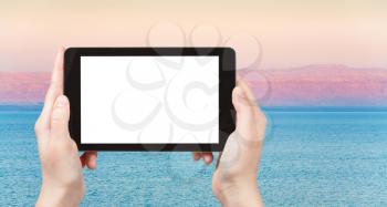 travel concept - tourist photographs pink sunrise over blue calm Dead Sea on tablet pc with cut out screen with blank place for advertising