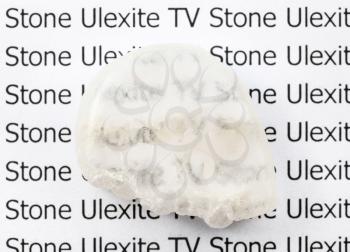 polished Ulexite (TV stone) natural mineral gemstone on sheet of paper with letter. Ulexite is known as TV rock due to fiber-optic effect: stone transmits light along fibers by internal reflection