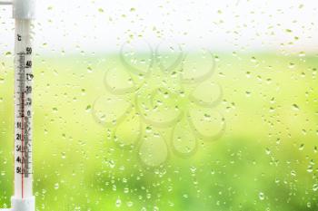 green background - raindrops on window pane and thermometer in summer day