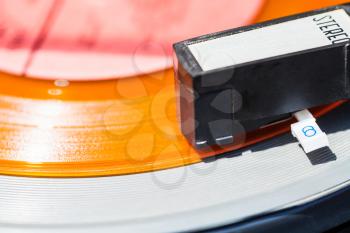 headshell of record-player on orange vinyl disc close up