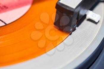 headshell of turntable on orange vinyl record close up