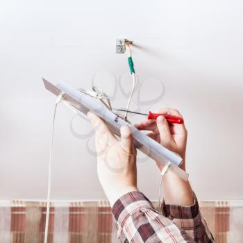 Electrician mounts wiring in ceiling lamp indoor