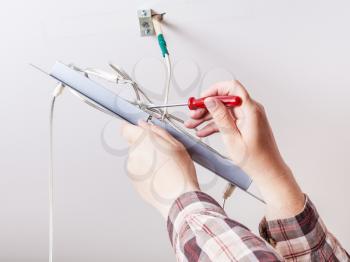 Electrician repairs wiring in ceiling lamp indoor
