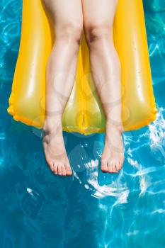 outdoor swimming pool - female legs on yellow air mattress in sunny summer day