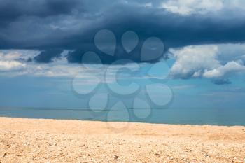 Foreground focus - landscape with sand beach and dark blue rain clouds over sea. Coastline of Sea of Azov, Temryuk bay, Golubitskaya resort, Taman peninsula, Kuban, Russia