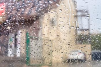 driving car in rain - rain trickles on windscreen and blurred house on background