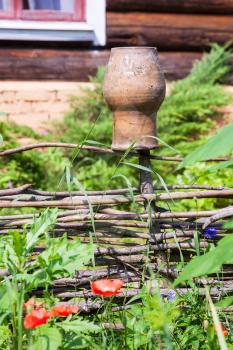 rural scenery - wattle hurdle with old clay pot and country log house