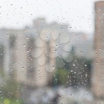 rain drops on window glass and blurred urban houses on background
