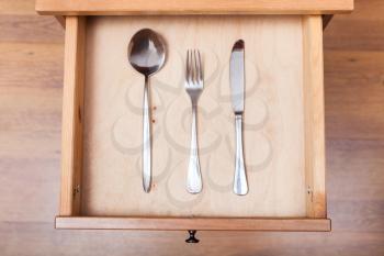 above view of table knife, fork, spoon in open drawer of nightstand