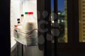Open door of home fridge with milk bottles in night
