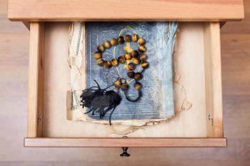 top view of rosary on old religious book in open drawer of nightstand
