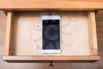 above view of mobile phone in open drawer of nightstand
