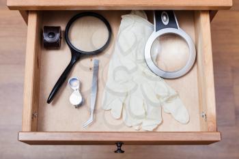 top view of magnifier, forceps and gloves in open drawer of nightstand