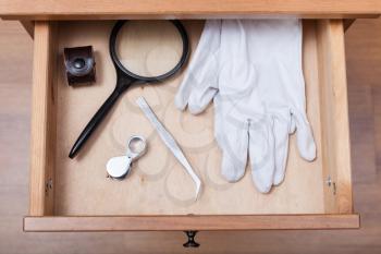 top view of magnifying glasses, tweezers and gloves in open drawer of nightstand