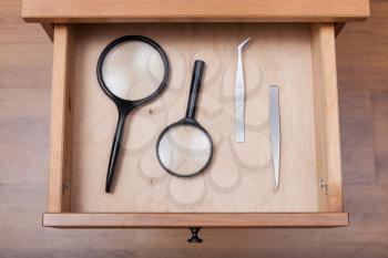 top view of magnifying glasses and tweezers in open drawer of nightstand