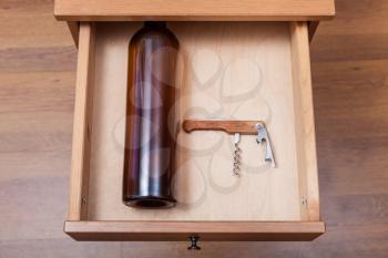 top view of empty wine bottle and corkscrew in open drawer of nightstand