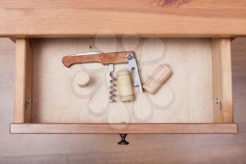 top view of foldable corkscrew and corks in open drawer of nightstand