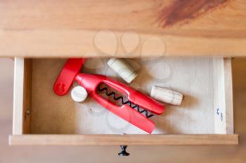 top view of corkscrew and cork from wine bottles in open drawer of nightstand