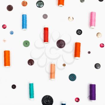spools of sewing thread and different buttons on square white background