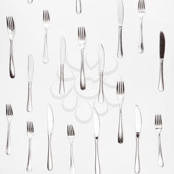 table knives and forks arranged on white square background