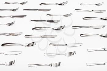 side view of many table knives and forks on white background
