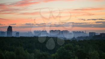 early sunrise and morning mist over woods and city in summer