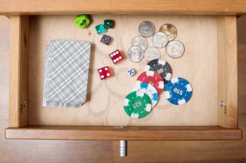 top view of deck of playing cards, dices, casino chips and coins in open drawer of nightstand