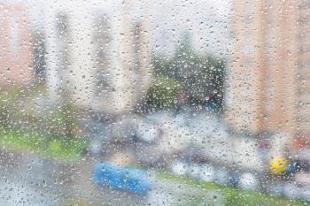 rainy weather in city - view of raindrops on windowpane of urban house