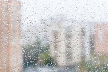 rainy weather in city - view of raindrops on window glass of urban house