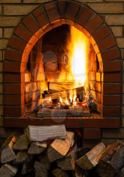 pile of wood and logs burning in indoor brick fireplace in country cottage