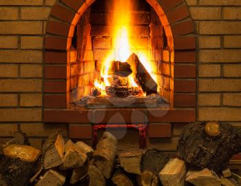 pile of firewood and tongues of fire in indoor brick fireplace in country cottage