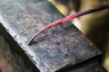 red hot glowing steel rod on anvil close up in smithy