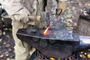 Blacksmith hammering hot steel rod on anvil in outdoor rural smithy