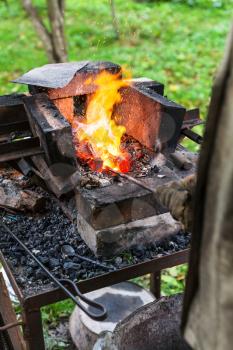 Blacksmith heats steel rod in rural forging furnace with burning coals