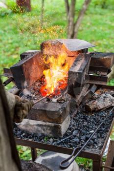 Blacksmith heats iron rod in rural forging furnace with burning coals