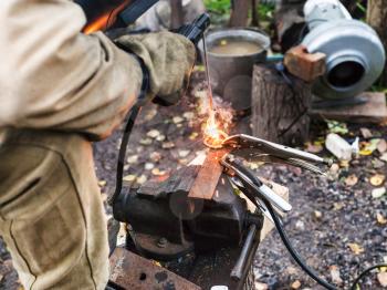 Welder welds steel buckle by spot electric welding in outdoor rural workshop