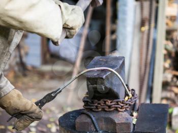 blacksmith forges iron rod on an anvil with a sledgehammer in outdoor rural smithy