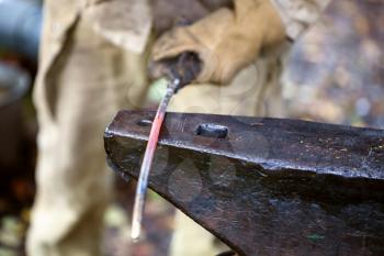 red hot glowing iron rod on anvil in outdoor rural smithy