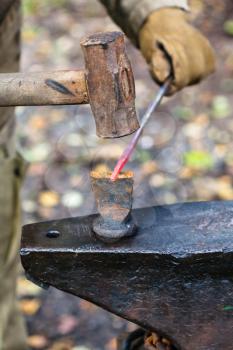 Blacksmith chops iron rod with hammer and chisel on anvil in outdoor rural smithy