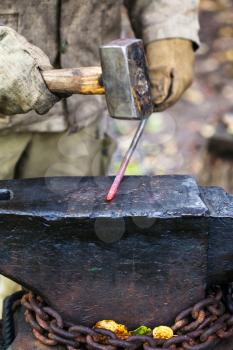 Blacksmith forges hot steel rod with sledgehammer on anvil in outdoor rural smithy