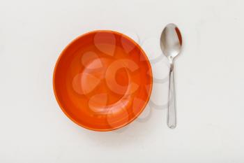 top view of orange bowl and spoon on white plastering plate