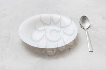 white deep plate and metal spoon on gray concrete board