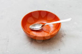 one orange bowl with spoon on gray concrete plate