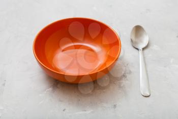one orange bowl and steel spoon on gray concrete plate