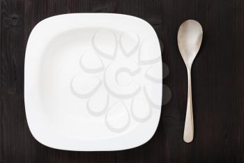 top view of one white bowl with spoon on dark brown table