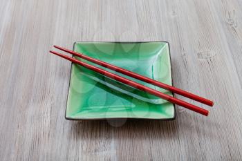 one green square saucer with red chopsticks on gray brown table