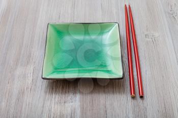 one green square saucer and red chopsticks on gray brown board